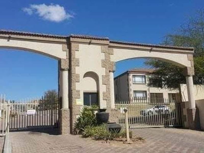 The main entrance to the apartment complex featuring a secure gated access point with stone-clad pillars and paved driveway.