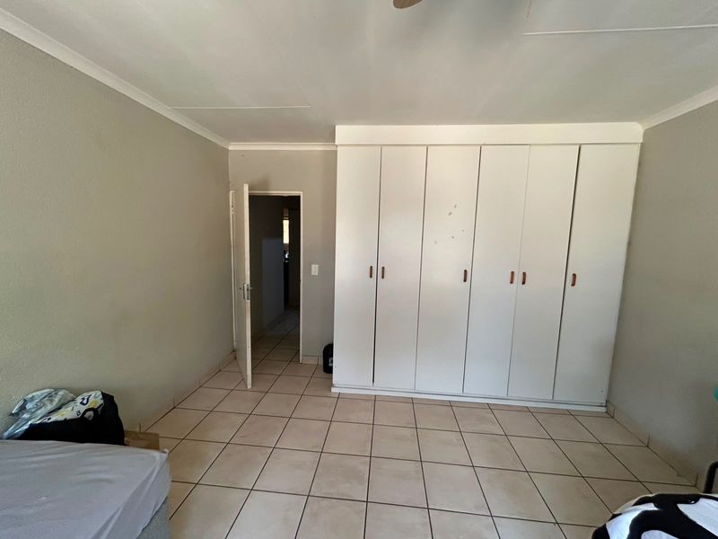 A bedroom featuring tiled flooring, a ceiling fan, and extensive built-in cupboard storage.