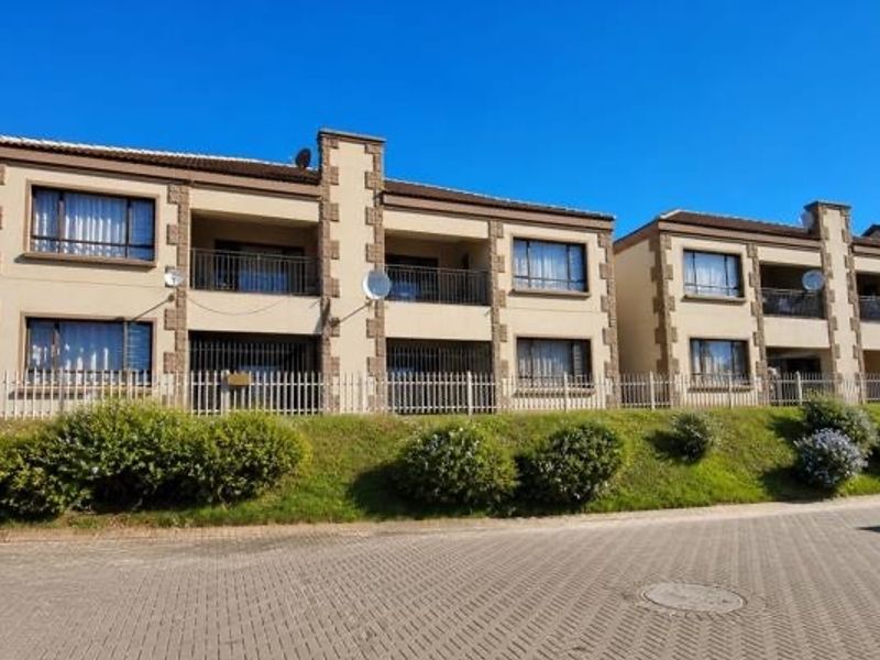 Front elevation of a multi-story apartment complex featuring balconies, paved driveway access, and secure perimeter fencing.