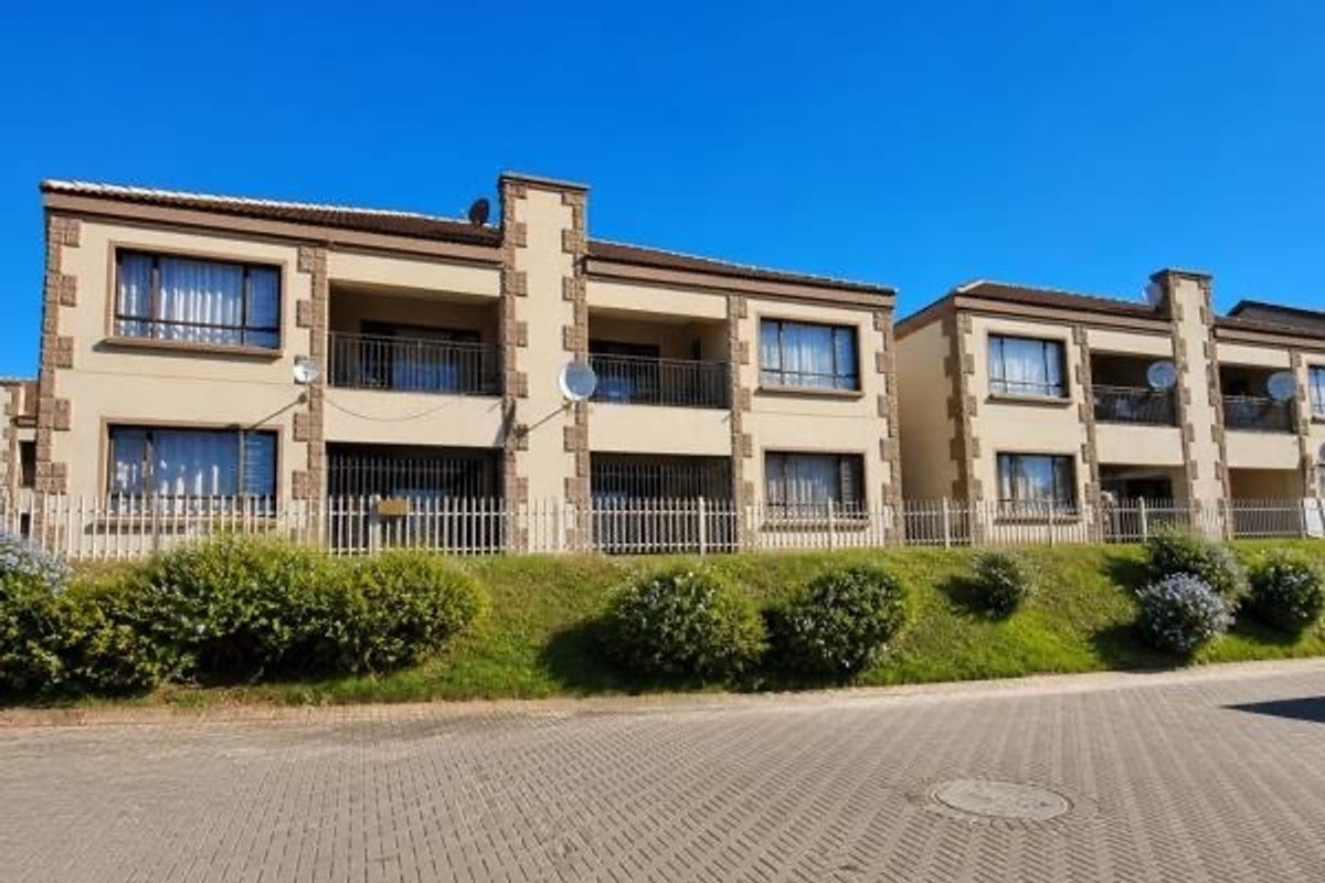Front elevation of a multi-story apartment complex featuring balconies, paved driveway access, and secure perimeter fencing.