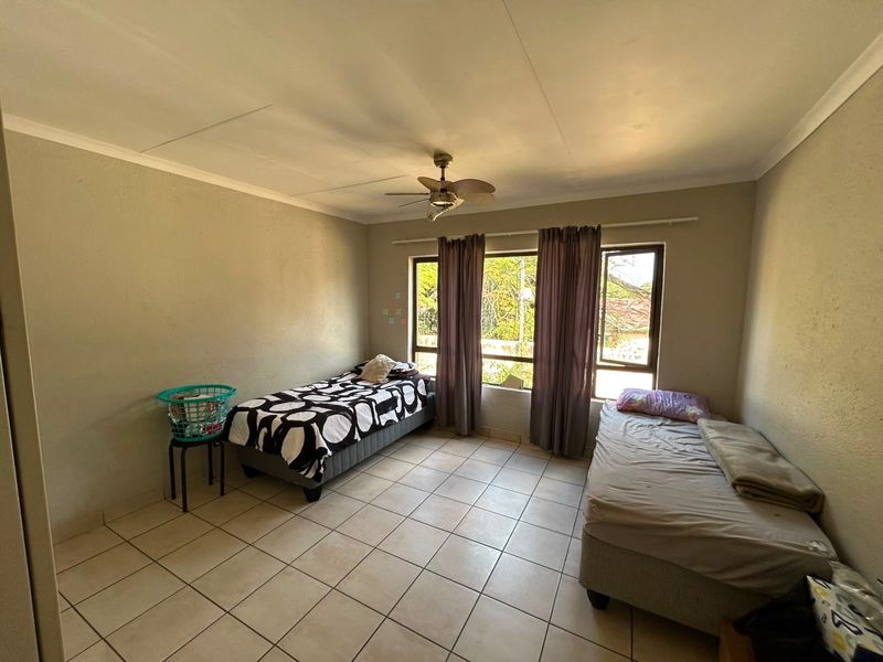 A bedroom featuring tiled flooring, a ceiling fan, and large windows that provide natural light.