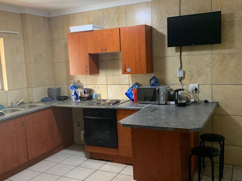Functional kitchen featuring wood-tone cabinetry, laminate countertops, built-in oven, electric hob, and full-height tiled splashbacks with neutral floor tiles.