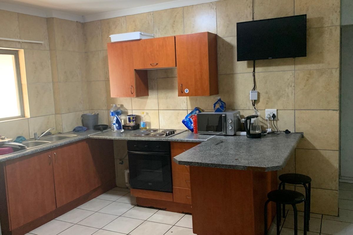 Functional kitchen featuring wood-tone cabinetry, laminate countertops, built-in oven, electric hob, and full-height tiled splashbacks with neutral floor tiles.