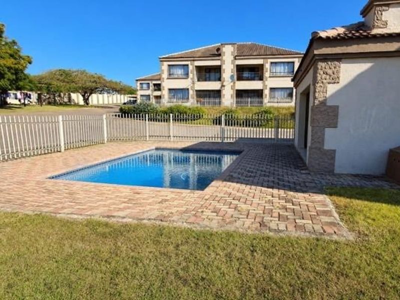 A well-maintained communal swimming pool area featuring paved surrounds and secure metal fencing, set within a residential apartment complex.