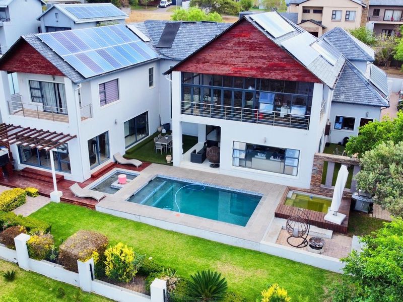 Aerial view of a modern multi-story residence featuring a swimming pool, timber decking, solar panels, and a well-maintained landscaped garden.