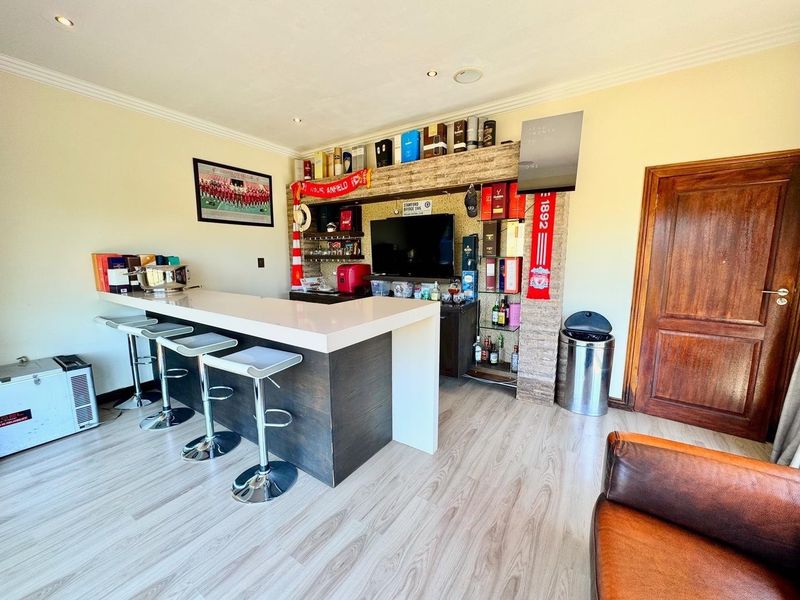 A dedicated home bar area featuring a modern built-in counter, stone-clad feature wall, recessed lighting, and durable laminate flooring.