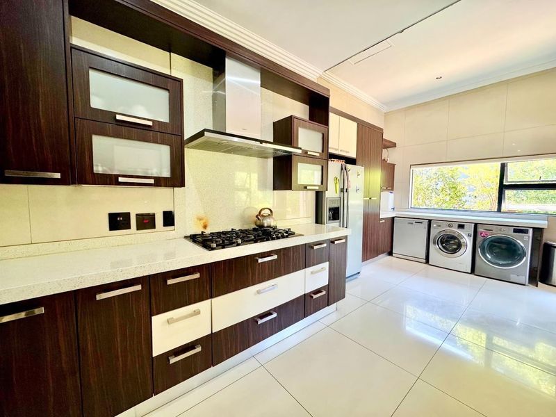 Modern kitchen featuring dark wood and white cabinetry, stone countertops, gas hob, extractor fan, and integrated laundry appliances with large format floor tiles.