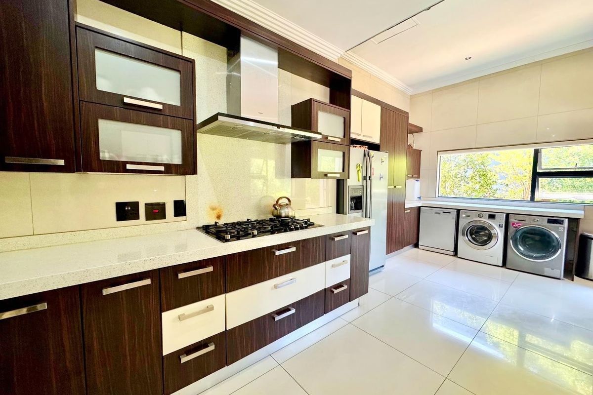 Modern kitchen featuring dark wood and white cabinetry, stone countertops, gas hob, extractor fan, and integrated laundry appliances with large format floor tiles.