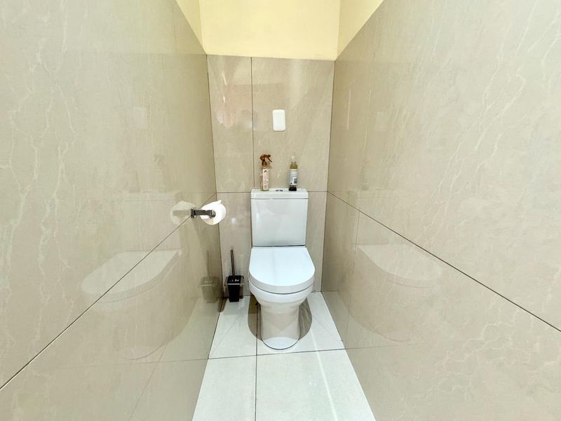 A compact, modern bathroom featuring full-height polished ceramic wall tiles and matching floor tiles, equipped with a standard white toilet.
