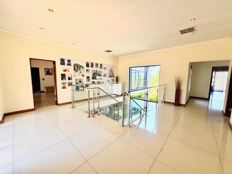 Spacious upper-level landing featuring polished tile flooring, a modern glass balustrade overlooking the staircase, and recessed lighting.