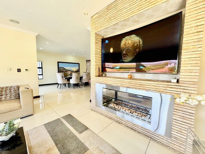 Spacious open-plan living area featuring a modern stone-clad feature wall with a built-in fireplace and integrated television mount, complemented by polished tiled flooring.