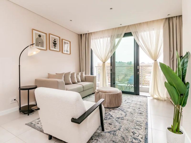 Bright and modern living room featuring large sliding glass doors leading to a balcony, neutral tiled flooring, and recessed ceiling lighting.