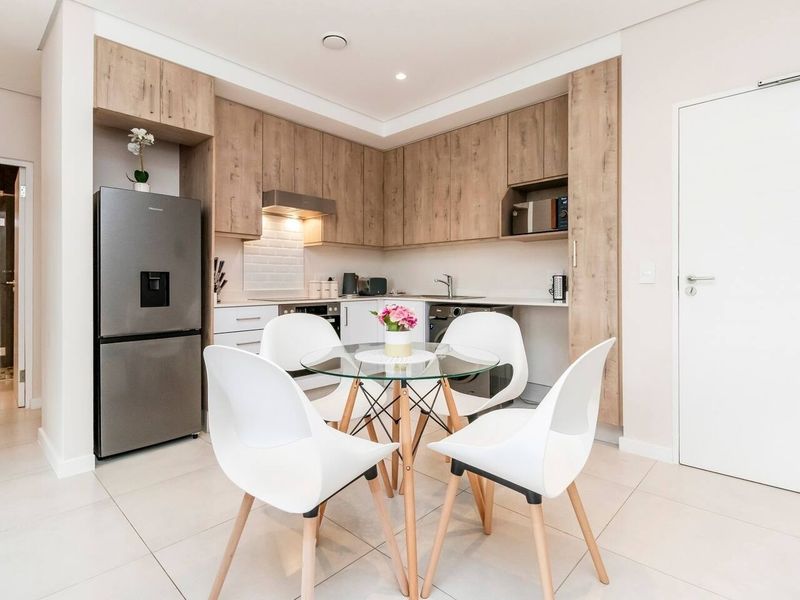 Modern open-plan kitchen featuring light wood-tone cabinetry, subway tile backsplash, and integrated appliances, seamlessly flowing into a bright dining area with tiled flooring.
