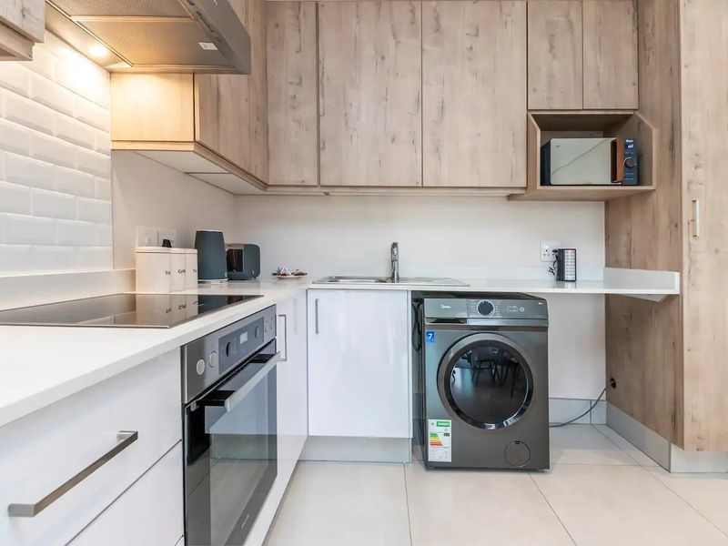 Modern kitchen featuring light wood-grain cabinetry, white quartz countertops, subway tile backsplash, integrated oven, electric hob, and a dedicated space for laundry appliances.