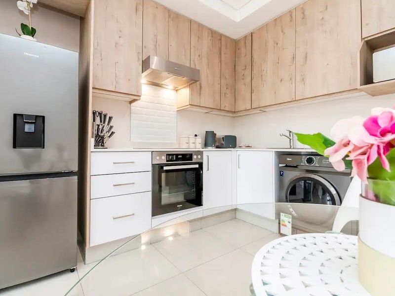 Modern kitchen featuring light wood-tone cabinetry, white subway tile backsplash, built-in oven, extractor fan, and integrated laundry appliance.