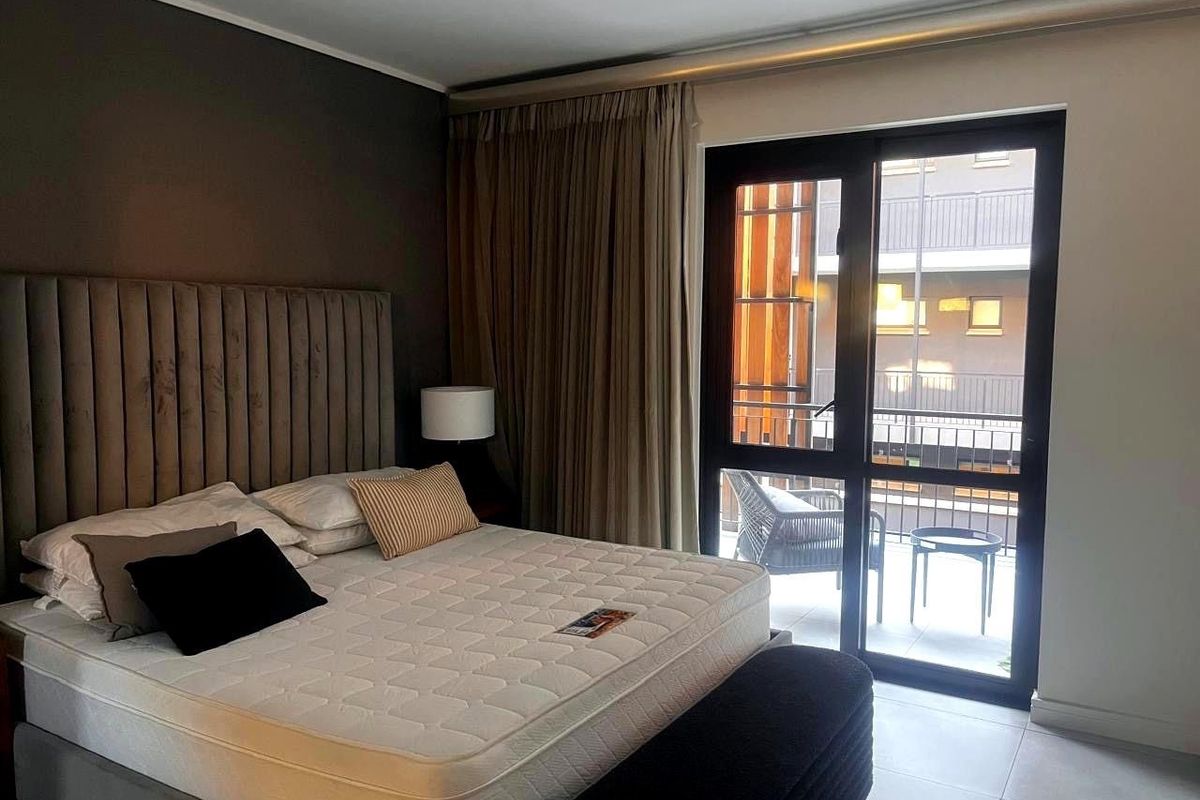 A modern bedroom featuring tiled flooring, a large upholstered headboard, and a sliding glass door providing access to a private balcony.