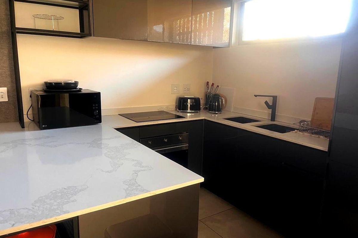 Modern kitchen featuring sleek dark cabinetry, stone countertops, integrated hob, built-in oven, and a double sink with contemporary fixtures.