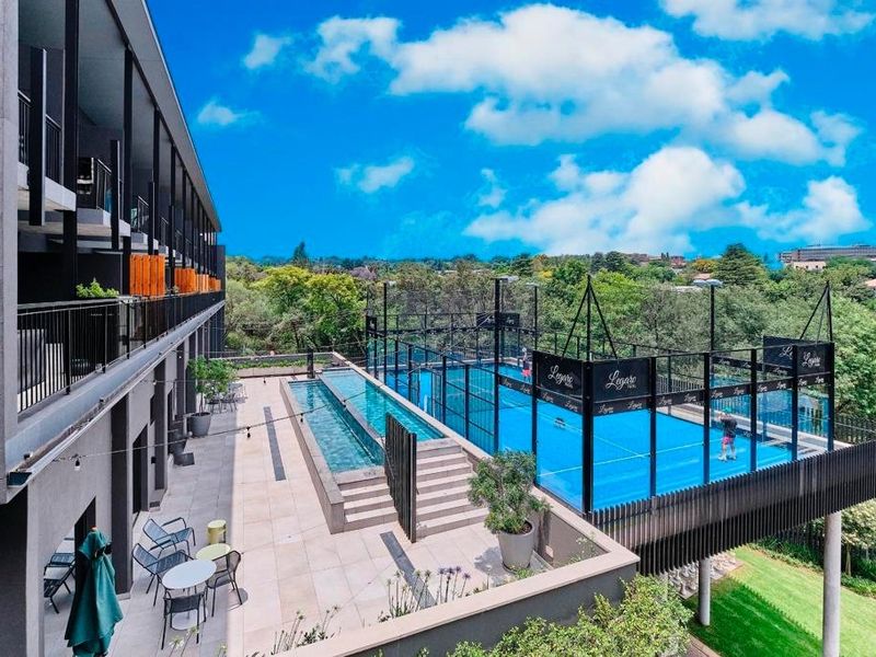 Modern apartment complex featuring a rooftop terrace with a swimming pool and a professional padel court overlooking the surrounding landscape.