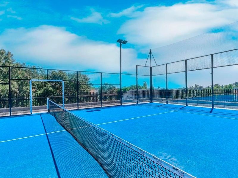 A well-maintained outdoor padel court featuring professional synthetic turf, perimeter fencing, and integrated floodlighting for evening play.