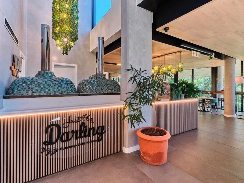 A modern commercial interior space featuring wood slat paneling, concrete structural columns, large windows, and tiled flooring, currently configured as a cafe.