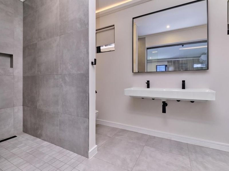 Modern bathroom featuring a spacious walk-in shower with grey tiling, a sleek wall-mounted double vanity, and a large black-framed mirror.