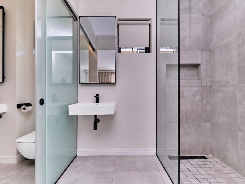 Modern bathroom featuring a wall-mounted basin, walk-in shower with glass screen, recessed niche, and wall-hung toilet with contemporary black fixtures.