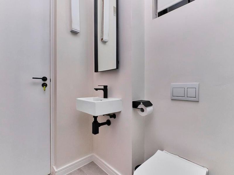 A modern, minimalist powder room featuring a wall-mounted basin, wall-hung toilet with concealed cistern, and sleek black fixtures.