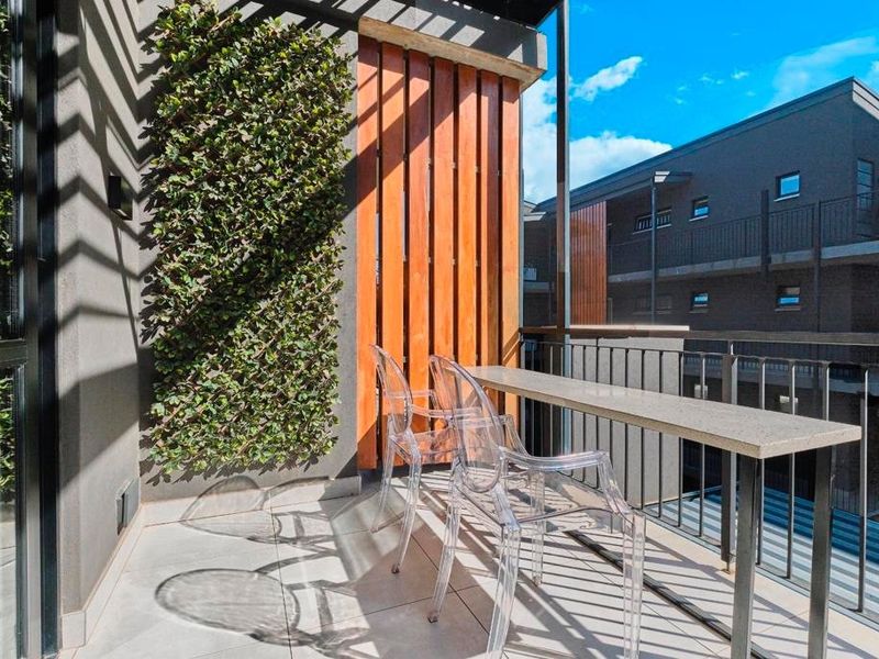 A modern apartment balcony featuring tiled flooring, a vertical timber privacy screen, and a fixed metal railing with views of the surrounding complex.