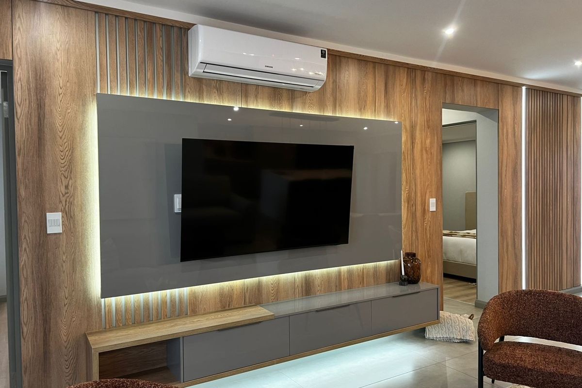 Modern living room featuring custom wood veneer wall paneling, integrated LED accent lighting, a sleek built-in media console, and a wall-mounted air conditioning unit.