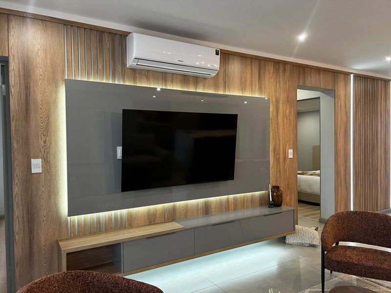 Modern living room featuring custom wood veneer wall paneling, integrated LED accent lighting, a sleek built-in media console, and a wall-mounted air conditioning unit.