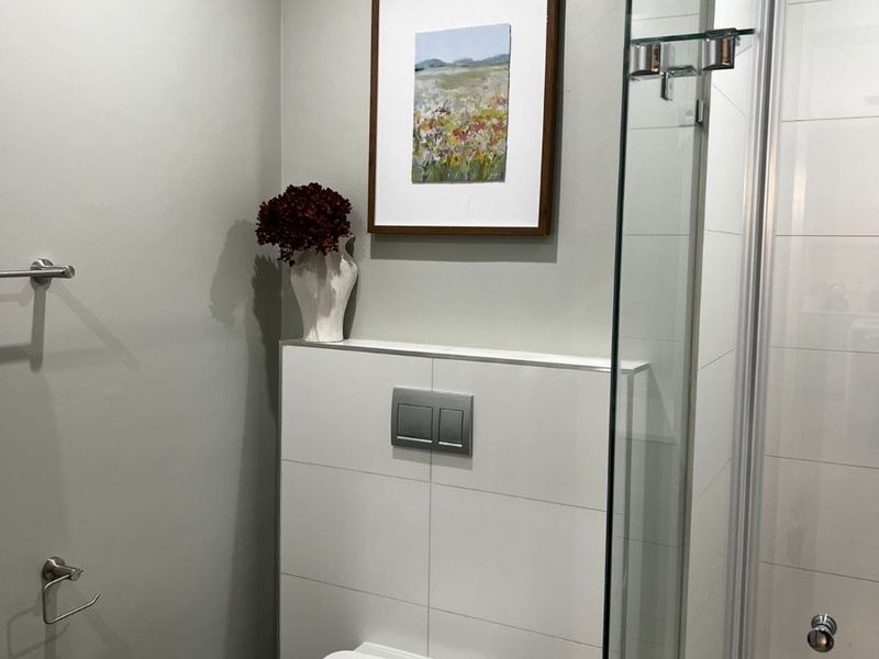 Modern bathroom featuring a wall-hung toilet with a concealed cistern and a sleek glass-enclosed shower area with neutral wall finishes.