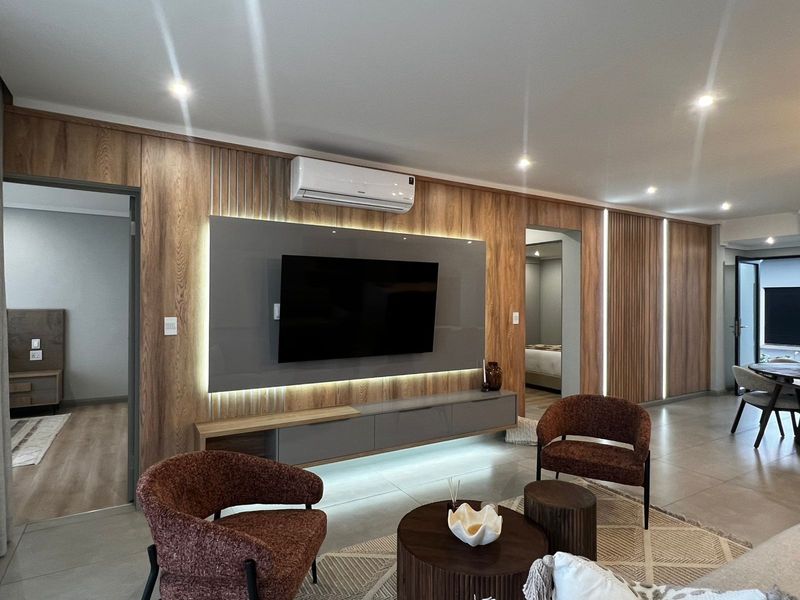 Modern living room featuring wood-paneled walls, integrated media console with ambient lighting, and split-system air conditioning.