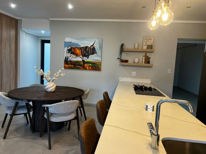 Modern open-plan kitchen and dining area featuring a stone-topped island with integrated gas hob, sleek cabinetry, and contemporary pendant lighting.