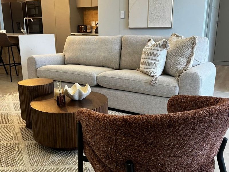 Modern open-plan living area featuring a sleek kitchen with island, neutral cabinetry, and contemporary lighting, seamlessly flowing into the comfortable lounge space.