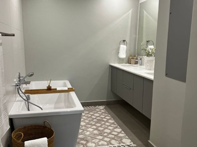 Modern bathroom featuring a sleek freestanding bathtub, wall-mounted double vanity, and contemporary tiled finishes with recessed lighting.