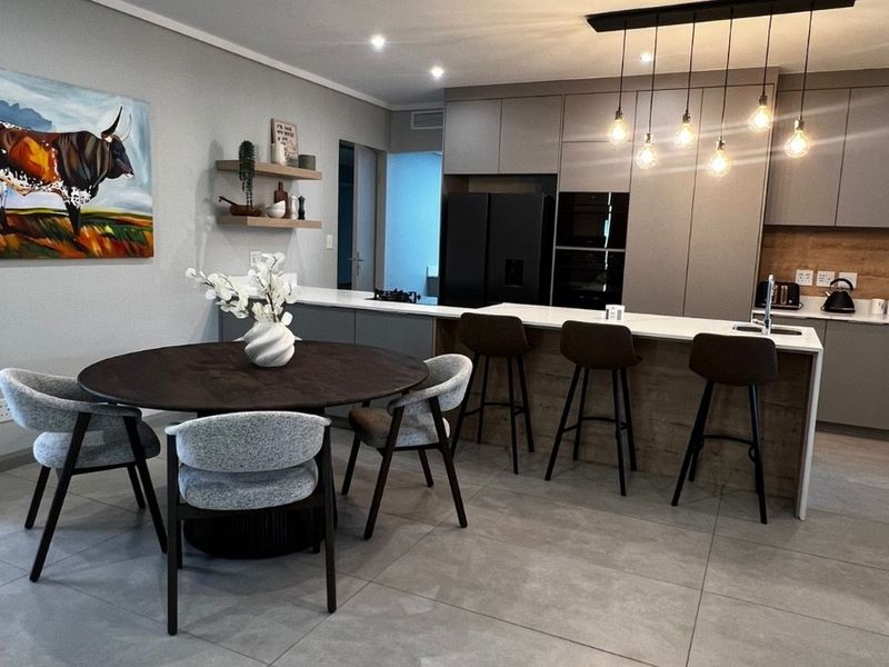 Modern open-plan kitchen and dining area featuring sleek cabinetry, a central island with breakfast bar, and contemporary lighting finishes.