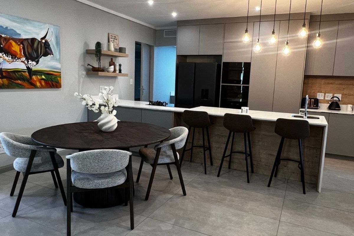 Modern open-plan kitchen and dining area featuring sleek cabinetry, a central island with breakfast bar, and contemporary lighting finishes.