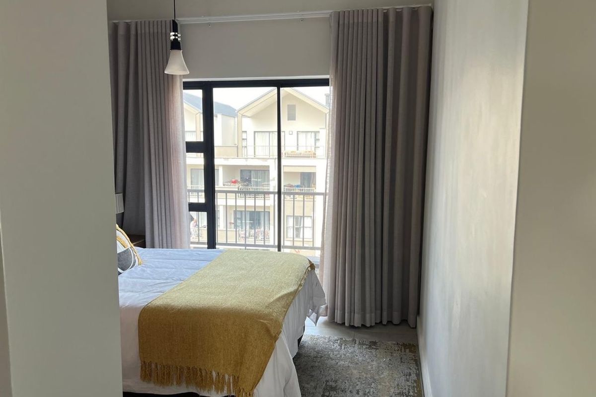 A well-lit bedroom featuring a sliding glass door with floor-to-ceiling curtains, providing access to an outdoor balcony area.