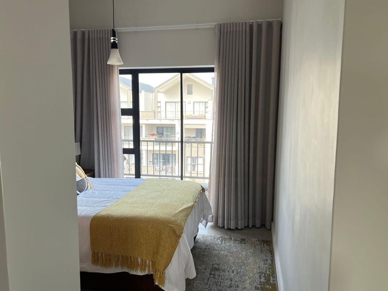 A well-lit bedroom featuring a sliding glass door with floor-to-ceiling curtains, providing access to an outdoor balcony area.