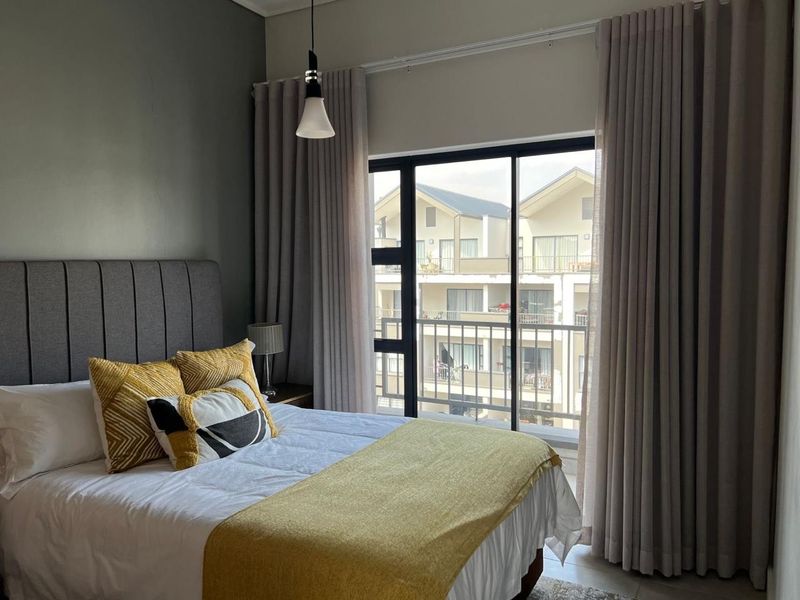 A well-maintained bedroom featuring a large sliding glass door with floor-to-ceiling curtains, providing natural light and access to an exterior balcony.