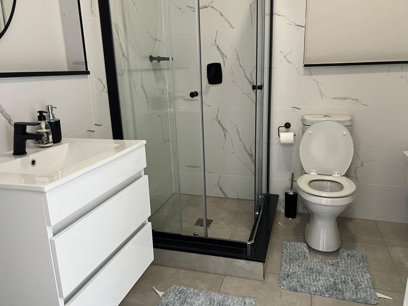 Modern bathroom featuring a vanity cabinet, glass shower enclosure, and marble-look wall tiles with contemporary black fixtures.