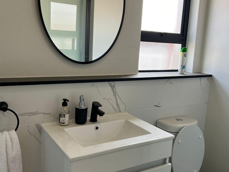 Modern bathroom featuring a vanity cabinet with a ceramic basin, black mixer tap, marble-look wall tiles, and a sleek black-framed mirror.