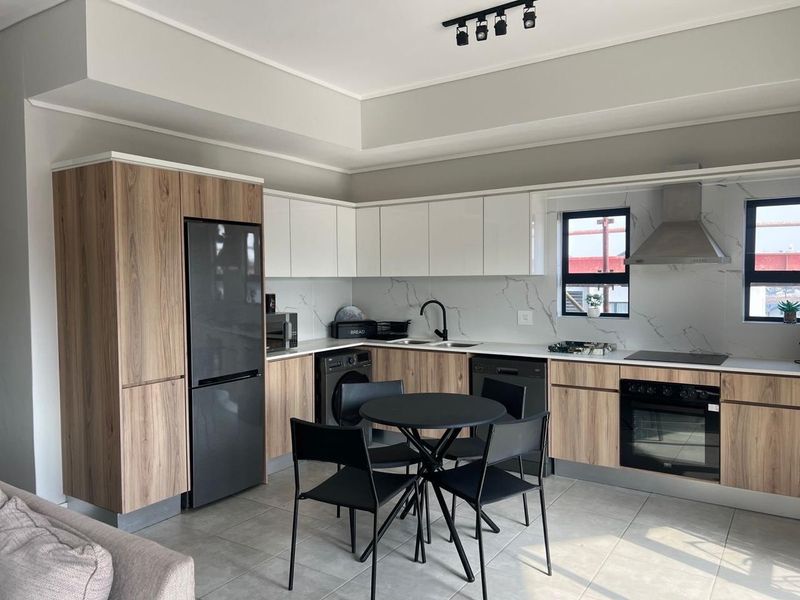 Modern open-plan kitchen featuring wood-grain and white cabinetry, marble-look splashback, integrated appliances, and sleek track lighting in a well-maintained apartment setting.