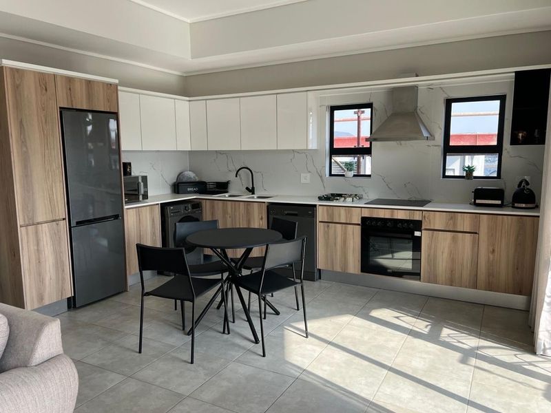Modern kitchen featuring wood-grain and white cabinetry, stone-look backsplash, integrated appliances, and sleek black fixtures in an open-plan layout.