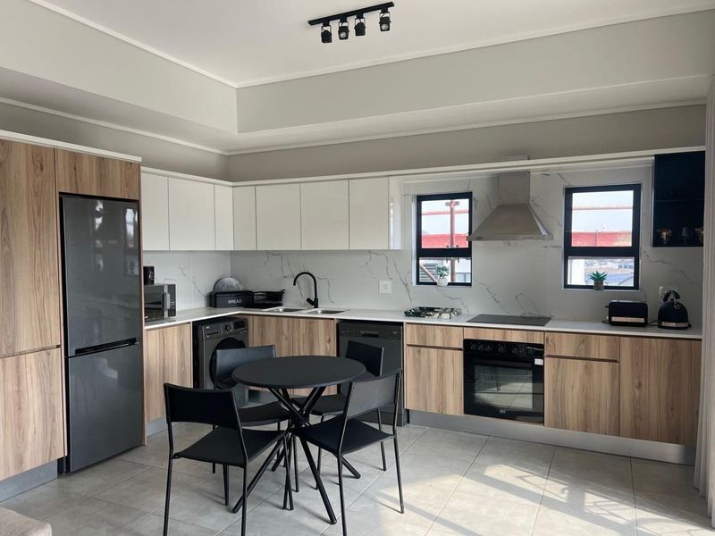 Modern kitchen featuring wood-grain and white cabinetry, stone-look backsplash, integrated oven, electric hob, and sleek track lighting in a well-maintained open-plan layout.