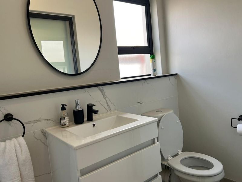 Modern bathroom featuring a white vanity cabinet with a basin, marble-look wall tiles, a round mirror, and contemporary black fixtures.