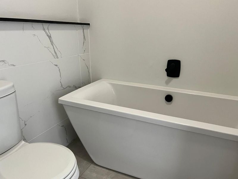 Modern bathroom featuring a sleek freestanding bathtub, contemporary black matte fixtures, and elegant marble-look wall tiling.