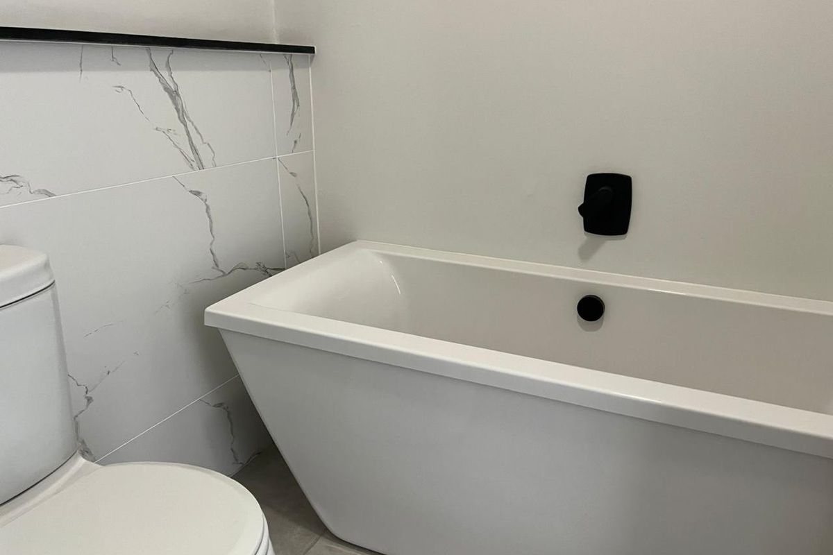 Modern bathroom featuring a sleek freestanding bathtub, contemporary black matte fixtures, and elegant marble-look wall tiling.