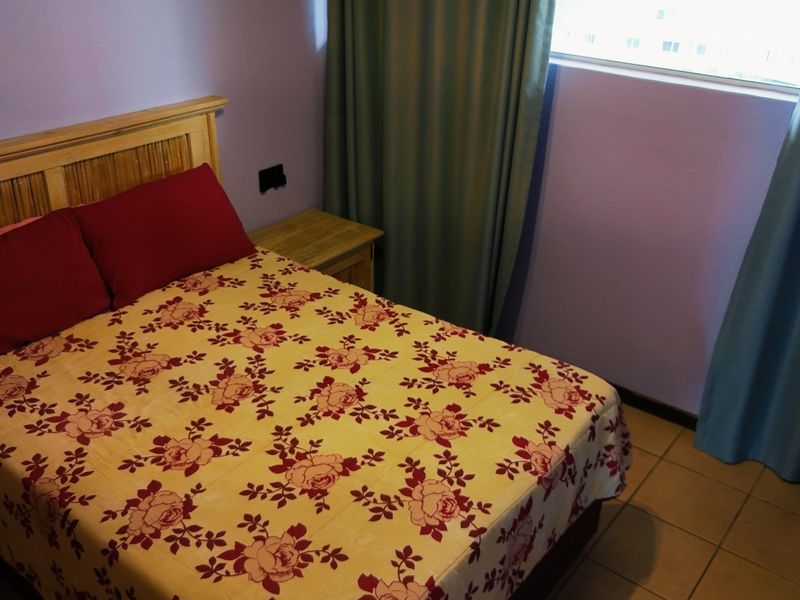A bedroom featuring tiled flooring and a window with curtains, providing a functional space with neutral wall finishes.