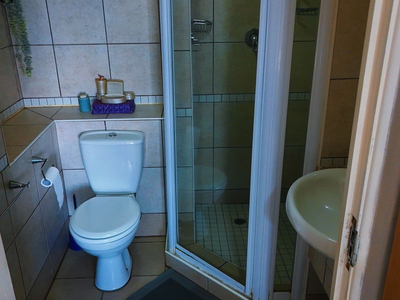 A functional bathroom featuring a corner shower enclosure, a standard toilet, and a pedestal basin with neutral wall and floor tiling.
